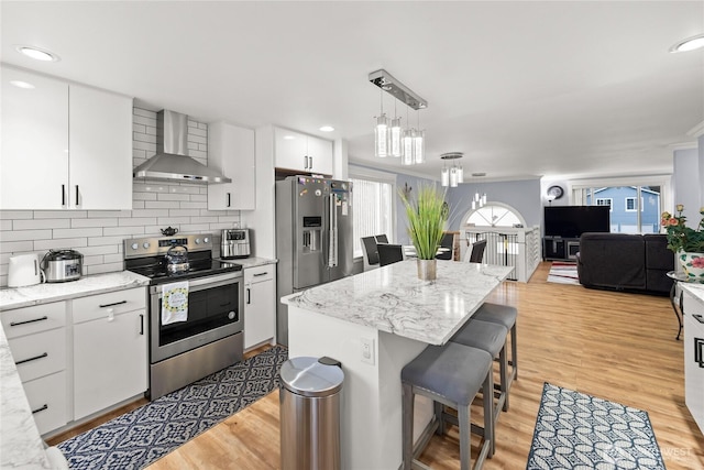 kitchen featuring light wood finished floors, decorative backsplash, appliances with stainless steel finishes, and wall chimney range hood