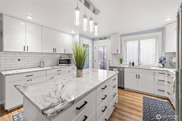 kitchen featuring a sink, light stone counters, a center island, light wood-style floors, and appliances with stainless steel finishes