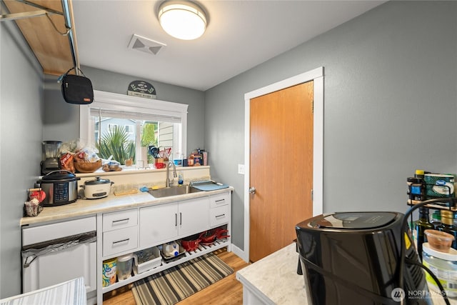 kitchen with visible vents, light wood-type flooring, a sink, white cabinets, and light countertops