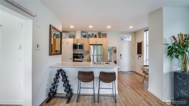 kitchen with tasteful backsplash, light wood finished floors, light countertops, appliances with stainless steel finishes, and a peninsula