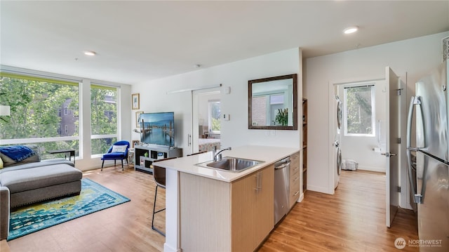 kitchen featuring light wood-type flooring, a breakfast bar, a sink, stainless steel appliances, and light countertops