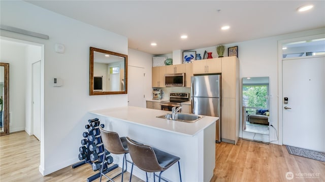 kitchen with light wood finished floors, a peninsula, a sink, appliances with stainless steel finishes, and a kitchen breakfast bar