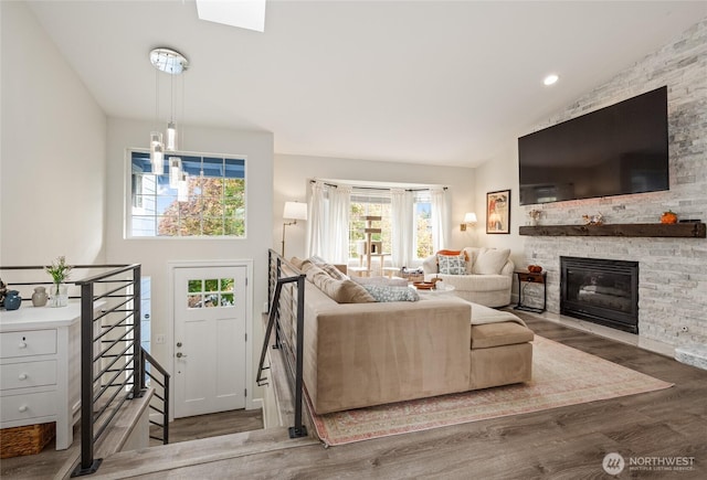 living area featuring high vaulted ceiling, a stone fireplace, and wood finished floors