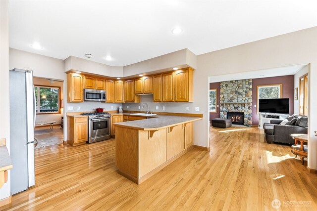 kitchen featuring light wood-type flooring, a peninsula, a sink, stainless steel appliances, and open floor plan