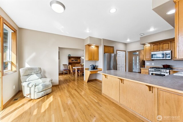 kitchen with visible vents, light wood-style flooring, a kitchen breakfast bar, a peninsula, and stainless steel appliances