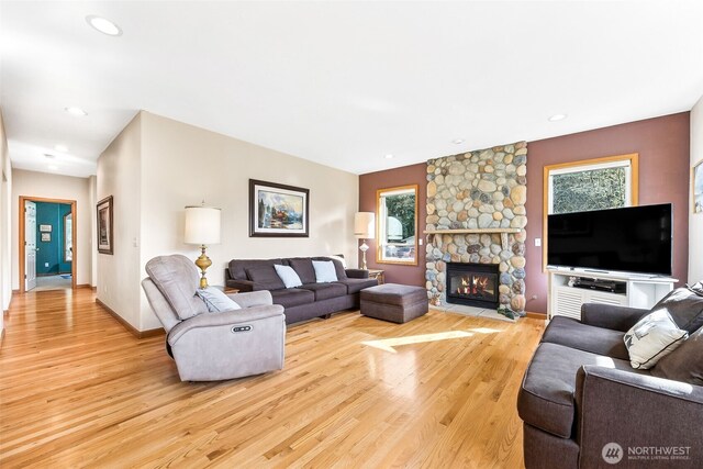 living room featuring a stone fireplace, recessed lighting, light wood-style floors, and baseboards