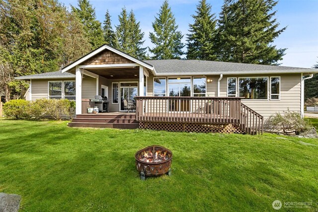 back of house featuring a yard, a fire pit, roof with shingles, and a wooden deck