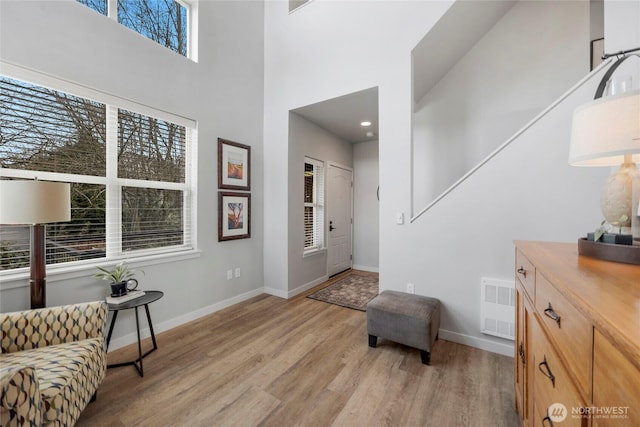 entryway featuring a towering ceiling, visible vents, baseboards, and light wood finished floors