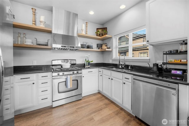 kitchen with dark countertops, open shelves, appliances with stainless steel finishes, wall chimney exhaust hood, and a sink