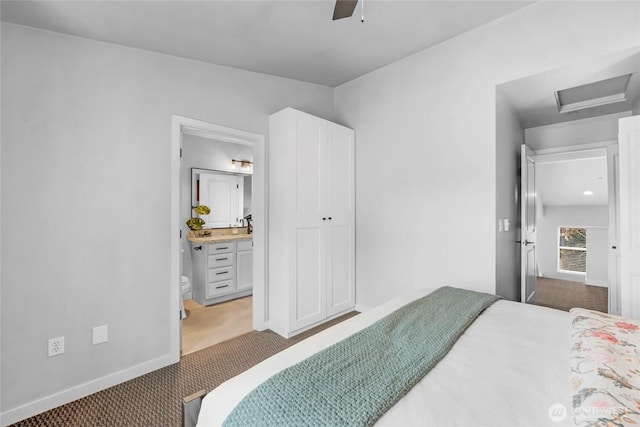 carpeted bedroom with baseboards, attic access, ensuite bath, and a ceiling fan