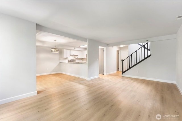 unfurnished living room featuring stairway, visible vents, baseboards, and light wood finished floors