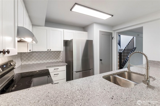 kitchen featuring ventilation hood, light stone counters, decorative backsplash, appliances with stainless steel finishes, and a sink