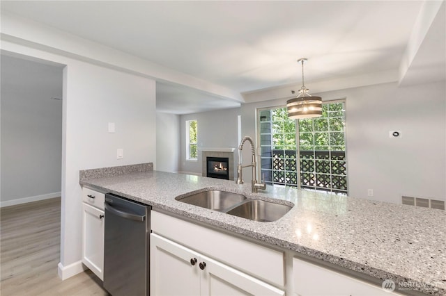 kitchen with stainless steel dishwasher, white cabinets, light stone counters, and a sink