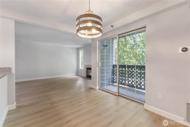 spare room featuring light wood finished floors, a glass covered fireplace, an inviting chandelier, and baseboards