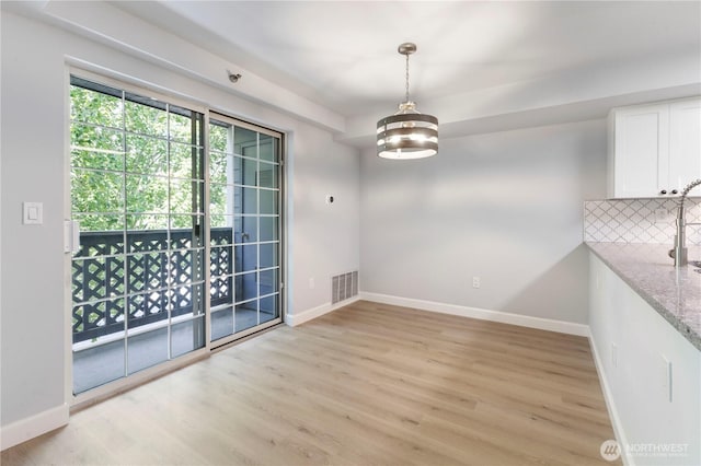 unfurnished dining area featuring baseboards, visible vents, and light wood finished floors