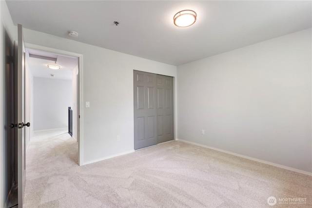 unfurnished bedroom with baseboards, a closet, and light carpet