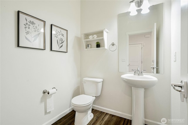 half bath featuring toilet, wood finished floors, baseboards, and a sink