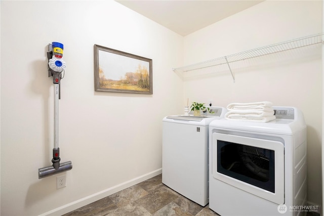 laundry room featuring laundry area, stone finish floor, separate washer and dryer, and baseboards