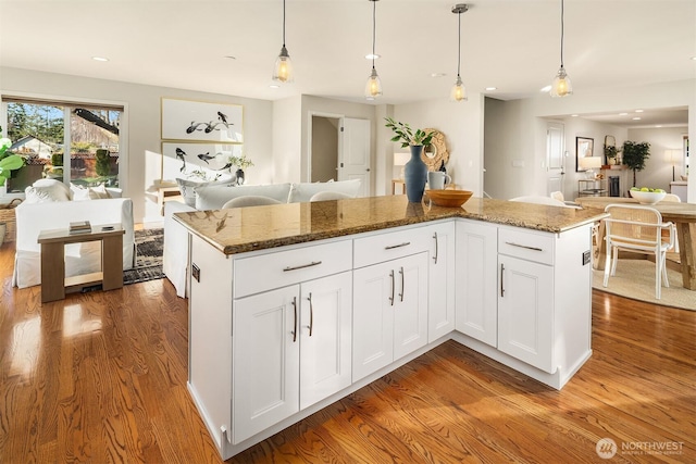 kitchen featuring stone countertops, pendant lighting, wood finished floors, and white cabinetry