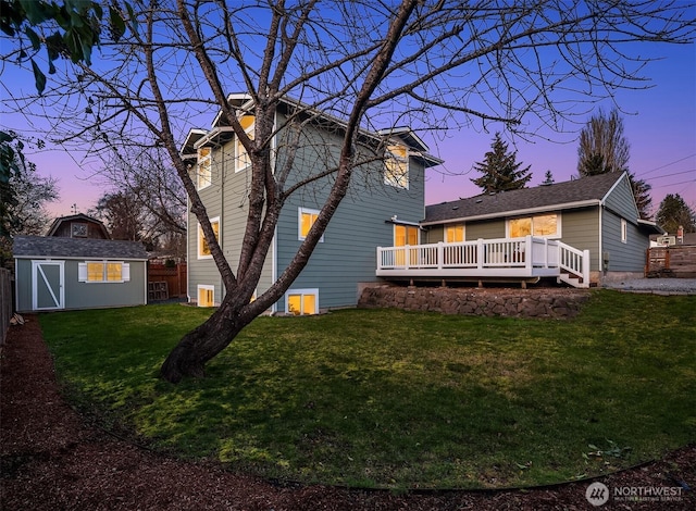 back of house at dusk featuring a deck, an outdoor structure, a storage unit, and a lawn