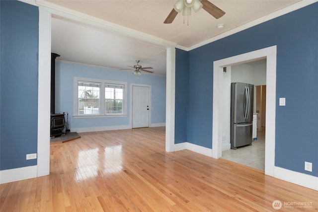 empty room featuring ceiling fan, a wood stove, and crown molding