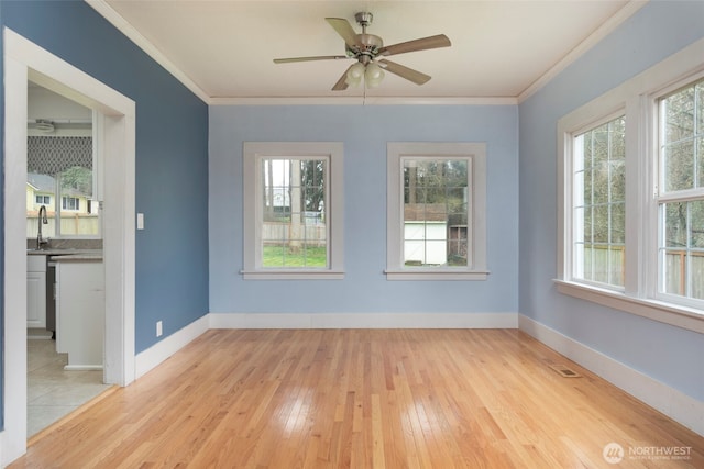 unfurnished room with a sink, light wood-type flooring, baseboards, and ornamental molding