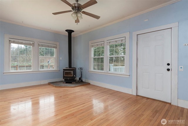 unfurnished living room featuring crown molding, a wood stove, baseboards, and hardwood / wood-style floors