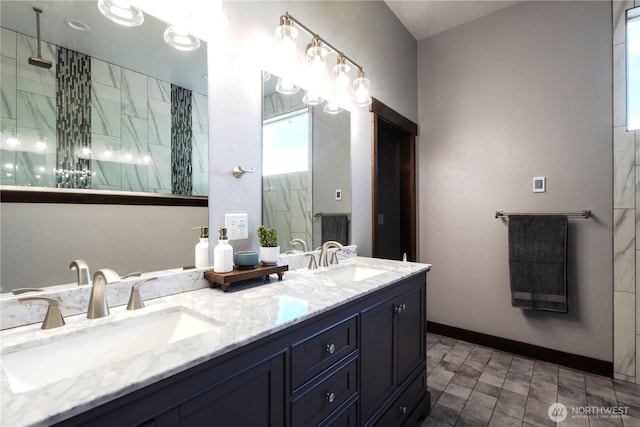 full bathroom featuring a sink, baseboards, tiled shower, and double vanity