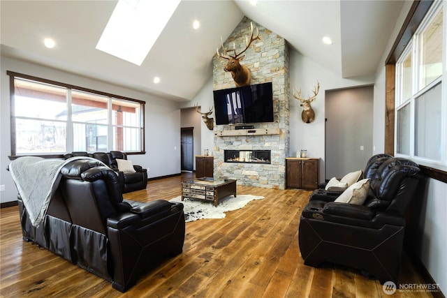 living room with a fireplace, a skylight, baseboards, and wood finished floors
