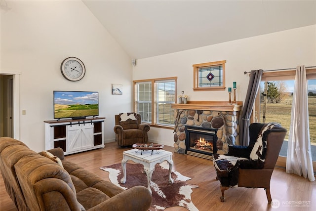 living room featuring baseboards, high vaulted ceiling, wood finished floors, and a fireplace