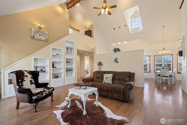 living room with built in shelves, baseboards, ceiling fan with notable chandelier, wood finished floors, and high vaulted ceiling