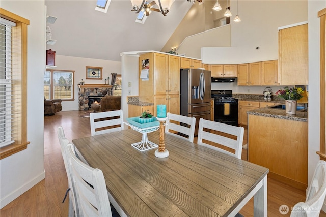 dining room with high vaulted ceiling, baseboards, light wood-style floors, and a fireplace