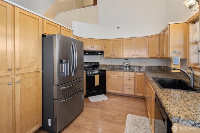 kitchen with light wood finished floors, under cabinet range hood, a high ceiling, black appliances, and a sink