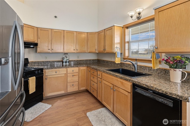 kitchen with black appliances, a sink, a high ceiling, exhaust hood, and light wood finished floors