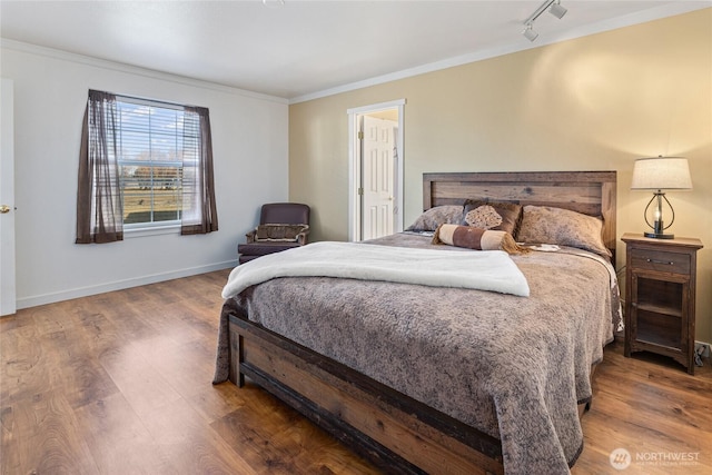 bedroom featuring rail lighting, wood finished floors, baseboards, and ornamental molding