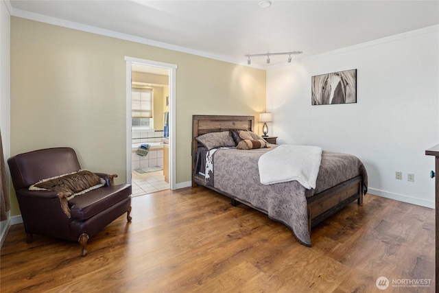 bedroom with ornamental molding, connected bathroom, baseboards, and wood finished floors