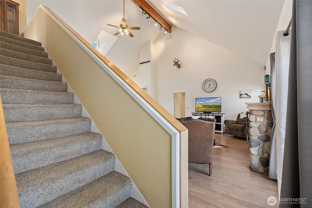 stairs featuring wood finished floors, high vaulted ceiling, a skylight, ceiling fan, and track lighting