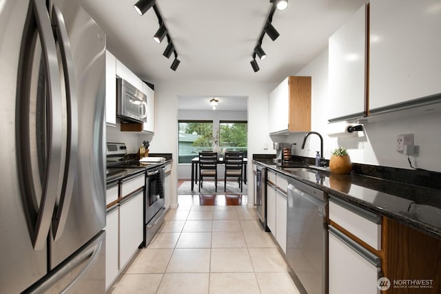 kitchen featuring dark stone counters, appliances with stainless steel finishes, light tile patterned flooring, white cabinets, and a sink