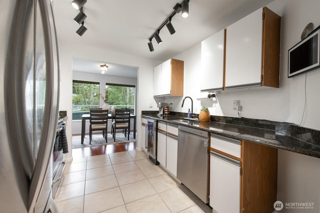 kitchen featuring a sink, white cabinetry, stainless steel appliances, dark stone counters, and light tile patterned floors