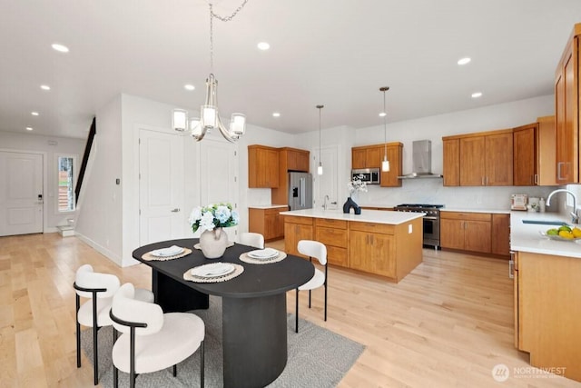 kitchen with brown cabinets, a sink, a kitchen island, appliances with stainless steel finishes, and wall chimney exhaust hood