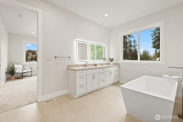 bathroom with visible vents, baseboards, double vanity, a soaking tub, and a sink