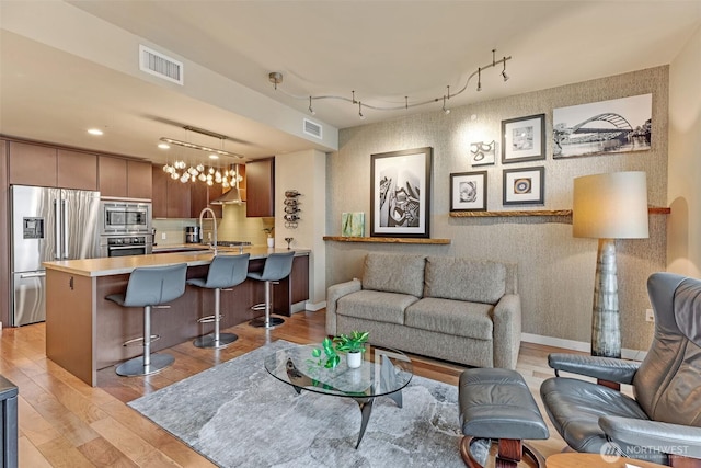 living room featuring wallpapered walls, baseboards, visible vents, and light wood-type flooring