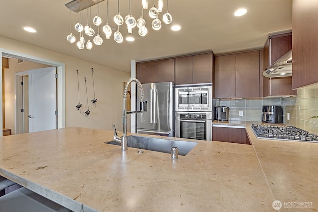 kitchen featuring under cabinet range hood, light stone countertops, stainless steel appliances, and tasteful backsplash