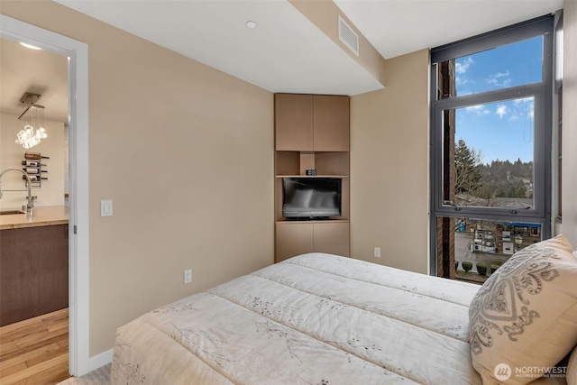 bedroom featuring a wall of windows, wood finished floors, baseboards, visible vents, and a sink