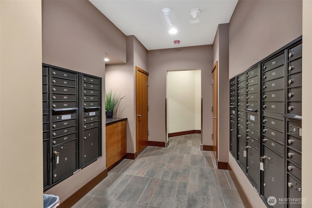 hall with mail area, baseboards, and stone finish floor