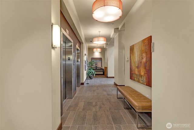 corridor with baseboards, elevator, and stone finish floor