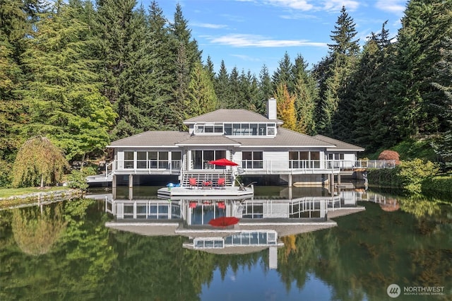 rear view of house featuring a wooded view, a chimney, a sunroom, and a water view