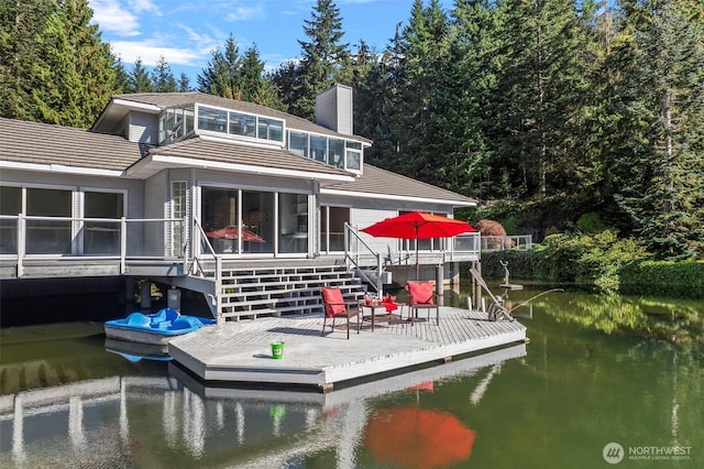 back of house featuring a tile roof, a water view, and a chimney