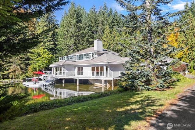 rear view of house with a yard, a water view, and a chimney