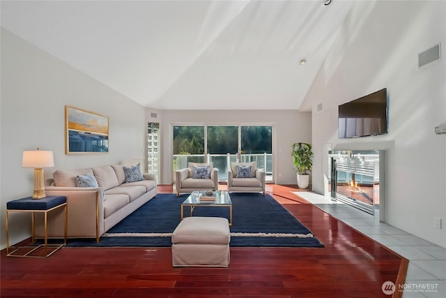 living room featuring a fireplace with flush hearth, wood finished floors, visible vents, and high vaulted ceiling